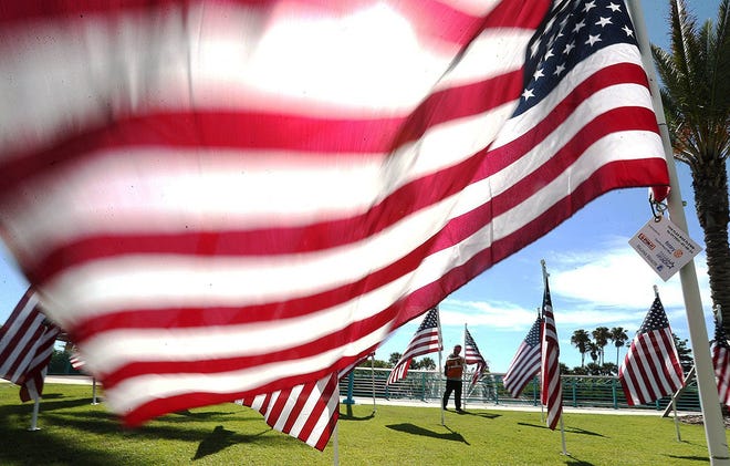 A man walks through the American Flag display at Veterans Plaza on Beach Street in Daytona Beach, Monday July 1, 2024 reading the name on the tags attached to the flags.