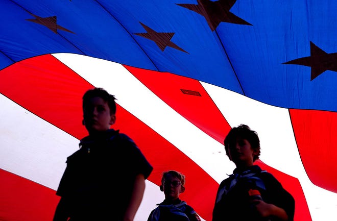 Scouts walk under a large American flag during the Edmond LibertyFest Parade in Edmond, Okla., Thursday, July, 4, 2024.