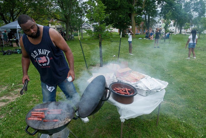 Thomas Giles grills hot dogs with his family as children play at Gordon Park in Milwaukee on Thursday, July 4, 2024.