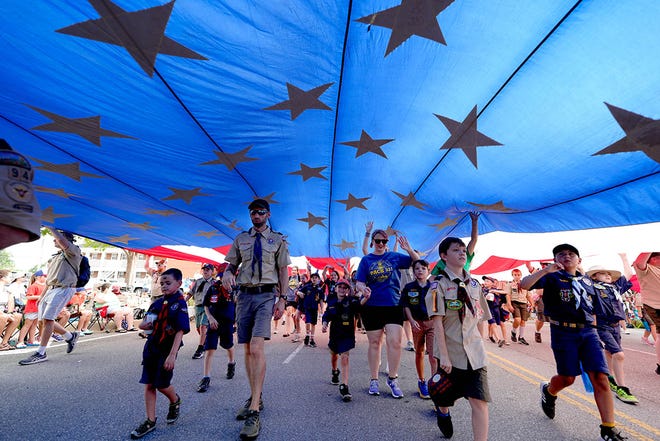 Scouts walk under a large American flag during the Edmond LibertyFest Parade in Edmond, Okla., Thursday, July, 4, 2024.